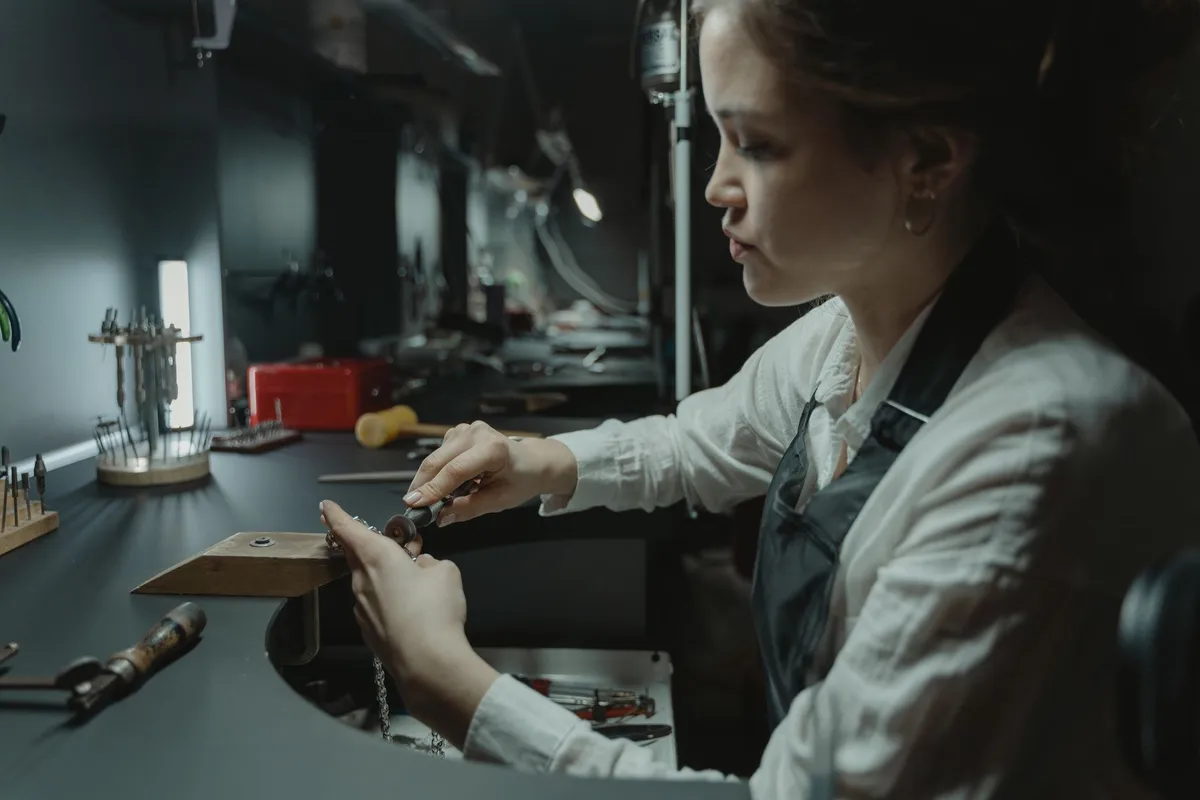 A skilled woman jeweler meticulously crafting jewelry in a workshop, highlighting craftsmanship in the industry.